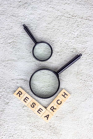Black magnifying glass with research text on light gray background. Statistic analyzing and scientific search concept.の写真素材