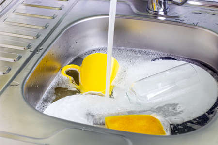 Metal sink in the kitchen full of dirty dishware stack. Housework, washing dishes, household duties concept.の写真素材