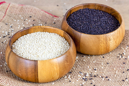 Black and white sesame seeds in wooden bowls for cooking on light textile background in the kitchen.
