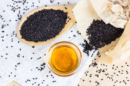 Black sesame seeds in a wooden spoon and oil on light background in the kitchen.の写真素材