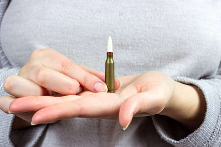 Caucasian woman hands holding a military gun bullet. War and conflict concept.の写真素材