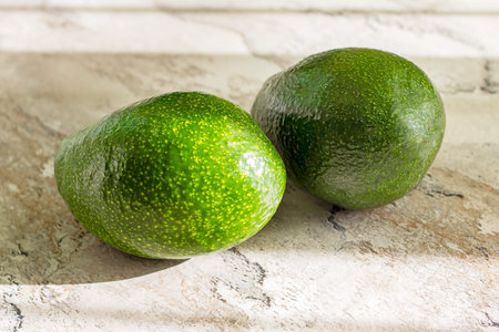 Two fresh green whole avocados on the table background in the kitchen.