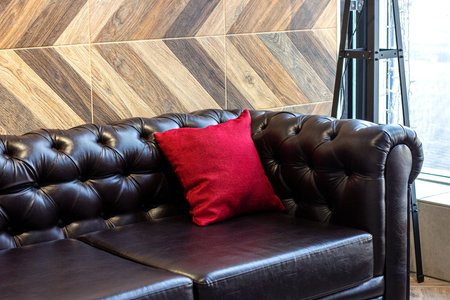 Big comfortable black leather sofa with red pillow in the furniture store.