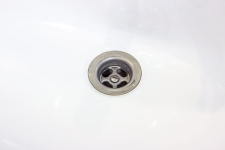 Metallic water drain hole in the white ceramic sink in the bathroom close up.の写真素材