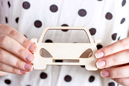 White wooden car toy miniature in Caucasian woman hands on light background. Automobile insurance, rent, sale and service concept.の写真素材