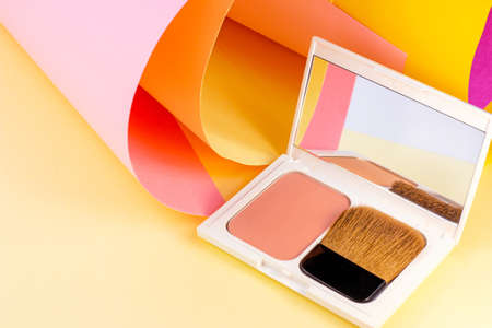 White plastic cosmetic container for cheek blusher on bright pink, orange and yellow background. Body and skin care, make-up and visage, wellness and beauty concept.の写真素材