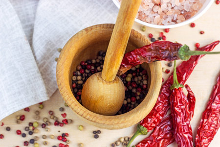 Top view of dried mixed peppercorns in the mortar with pestle, dry chili pepper and salt for cooking on light wooden cutting board background in the kitchen.の写真素材