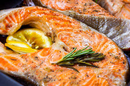 Fresh roasted red salmon fish steaks with herbs, spices and lemon on black metal plate background in the kitchen.の写真素材