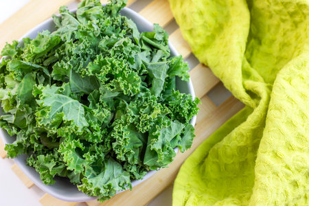 Top view of fresh green curly cabbage or kale salad leaves cut in the bowl on light background on...