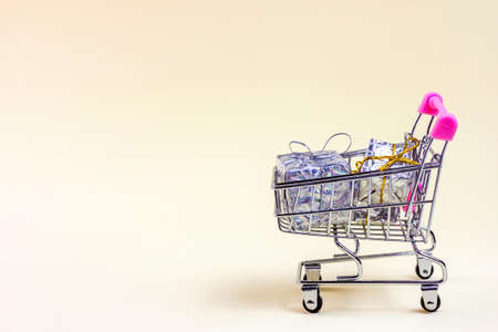 Trolley shopping cart with silver Xmas and Birthday boxes for gifts and presents on light background with copy space. Christmas sale, Black Friday and Cyber Monday discounts, holiday shopping concept.の写真素材