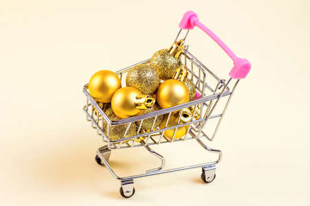 Trolley shopping cart with golden Xmas balls on light background. Christmas sale, discounts, holiday shopping and buying gifts and presents concept.の写真素材