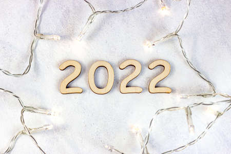 Wooden numbers 2022 silhouette with Christmas lights on light background. New Year beginning congratulations and planning concept.の写真素材