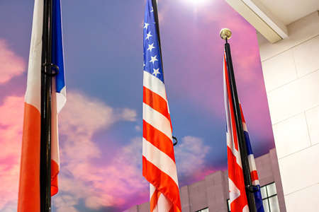 National flags of different countries (The United States of America, The United Kingdom and Russian Federation) against the colorful sky. Political union, diplomacy and global cooperation concept.の写真素材