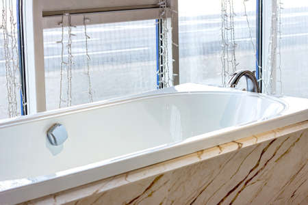 New modern empty white bathtub with water faucet and window in the bathroom.の写真素材