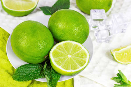 Fresh green juicy limes and lime slices with mint leaves in the kitchen on light background.の写真素材