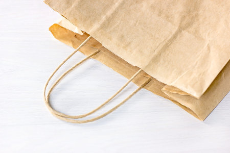 Beige craft paper bag on light wooden table with copy space. Eco-friendly zero waste recycling and disposable package for market purchases and home delivery.の写真素材