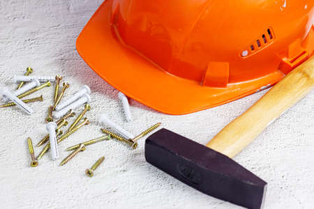 Orange protective hard hat with claw hammer on light gray cement. Home repairing and improvement, house building concept.の写真素材