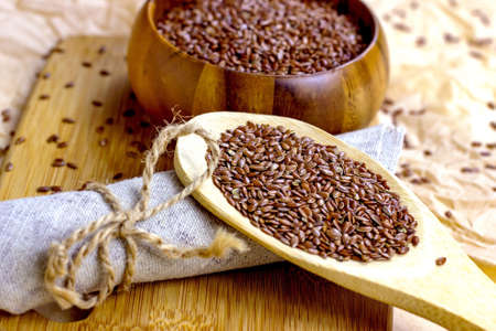 Brown raw dry flax seeds in a wooden spoon and bowl on a light background.の写真素材