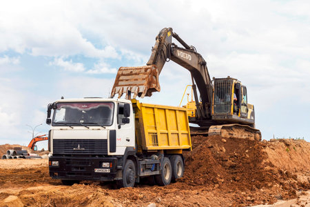 MINSK, BELARUS - July 2, 2021: Bright yellow heavy industrial excavator working on construction site...