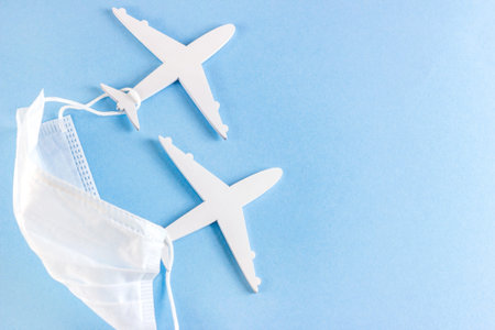 White planes with medical protective face mask on light blue background with copy space. Travelling...