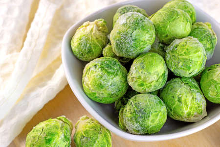 Many frozen whole brussels sprouts in white bowl on light wooden background.の写真素材