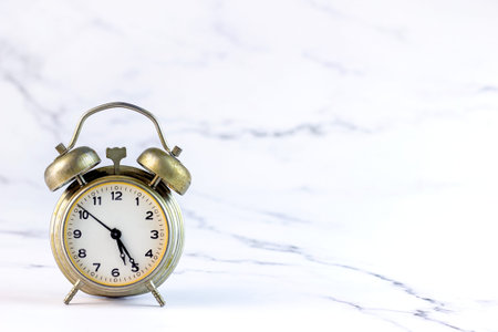 Round metal old analog retro alarm clock with black hour and minute hands on light marbled...