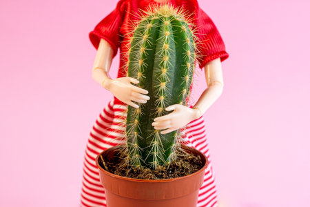 Woman doll hugs a cactus plant on light pink background. Harmful, painful and toxic relationship, partner problems, emotional abuse concept.の写真素材