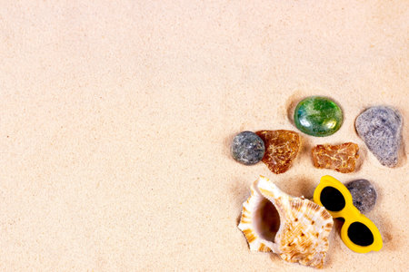 Yellow sandy textured background with bright seashells and stones as a frame with copy space top...