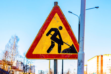 The bright orange warning Road Under Construction sign near the asphalt repair roadworks zone in the...