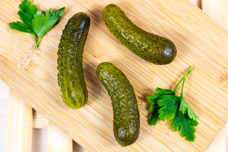 Tasty homemade green pickled cucumbers with fresh parsley on light wooden cutting board background in the kitchen.の写真素材