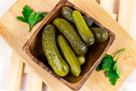 Tasty homemade green pickled cucumbers with fresh parsley in a wooden bowl on light cutting board background in the kitchen.の写真素材