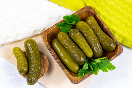 Top view of tasty homemade green pickled cucumbers with fresh parsley in a wooden bowl on light cutting board backgroundの写真素材