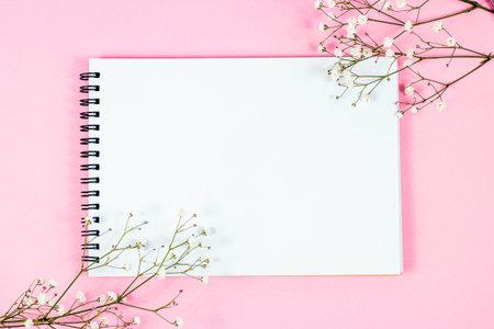 Whate blank notebook page with copy space for text with little flowers on pastel pink background top...