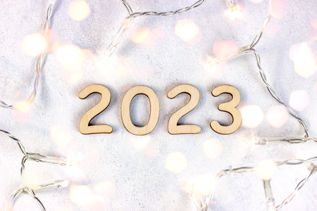 Wooden numbers 2023 silhouette with Christmas lights on light bokeh background. New Year beginning...
