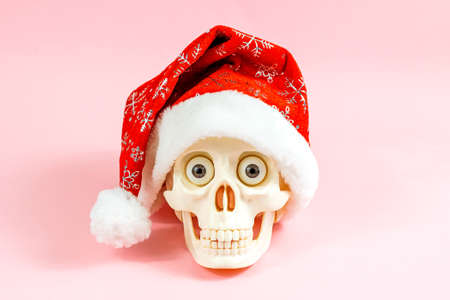 White skull in party xmas Santa Claus hat on light pink background. Christmas and New Year celebration concept.の写真素材