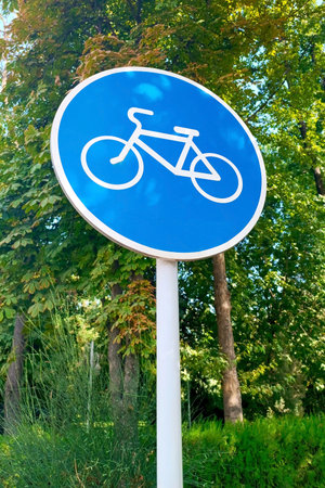 Blue and white bicycle lane sign indicating bike route, large round roadside traffic signage.