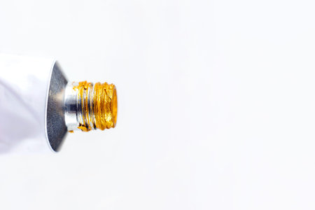 Metal acrylic tube with golden paint for drawing close up on white background with copy space.
