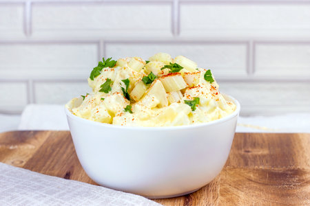 Fresh homemade traditional old-fashioned Amish Potato Salad with potatoes, boiled eggs, creamy dressing and celery in a white bowl on wooden background.の写真素材