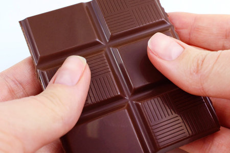 Caucasian woman hands holding and breaking off chocolate from a bar close up.