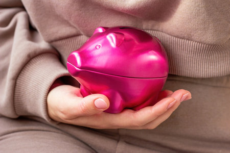 Woman hand holding bright pink pig money box close up. Economy, budget and savings concept.の写真素材