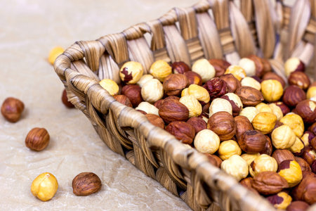 Peeled brown hazelnuts in wooden basket on light background.の写真素材