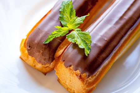 French pastry eclairs with cream filling covered with melted milk chocolate and mint leaves on a...