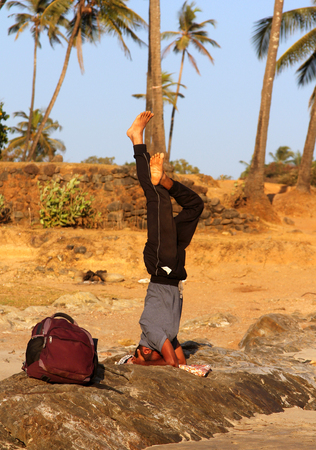 GOA, INDIA - FEB 10, 2014: Indian man standing on his head on the beach of Goa. Sirsasana pose is a "king" of yoga asanasのeditorial素材