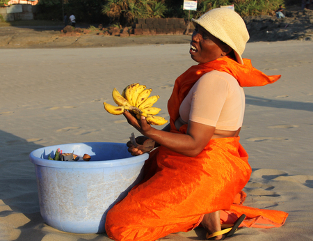 GOA, INDIA - FEB 16, 2014: Indian woman in beautiful orange sari selling fruits on the beach of Arabian seaのeditorial素材
