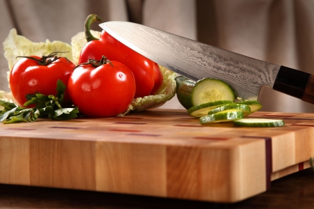 the knifed cucumber, tomatoes and pepper on a chopping boardの写真素材