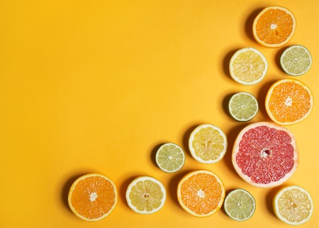 Cut citruses of different colors on yellow top view. Sliced lemon, orange, lime and grapefruit. Copy space for textの写真素材