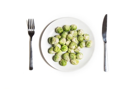 Diet vegetarian food isolated on white top view. Baby brussels sprouts on a plate with fork and knifeの写真素材