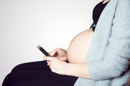 Pregnant woman sitting with smart phone and browsingの写真素材