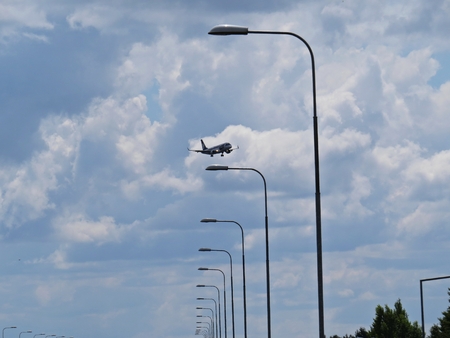 A Flying Plane Airplane of LOT Polish Airlines Together with a Street Lamp and Cloudy Sky, Warsaw, Poland, July 2018のeditorial素材