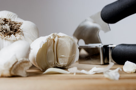 Garlic press and garlic cloves on a wooden cutting board closeupの写真素材
